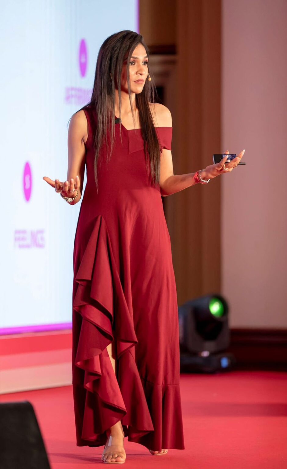 Riddhi speaking on stage in a red dress